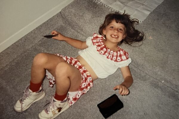 Maegan at 5 years old lying on the carpeted floor smiling up at the camera showing her missing front teeth