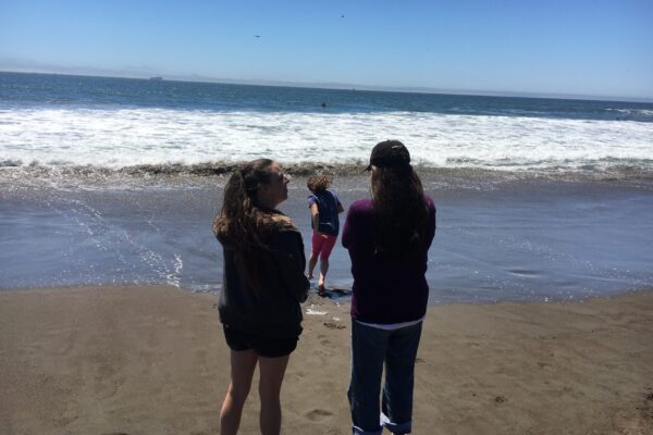 Maegan, Sara, and Stacey standing facing the water at the beach.